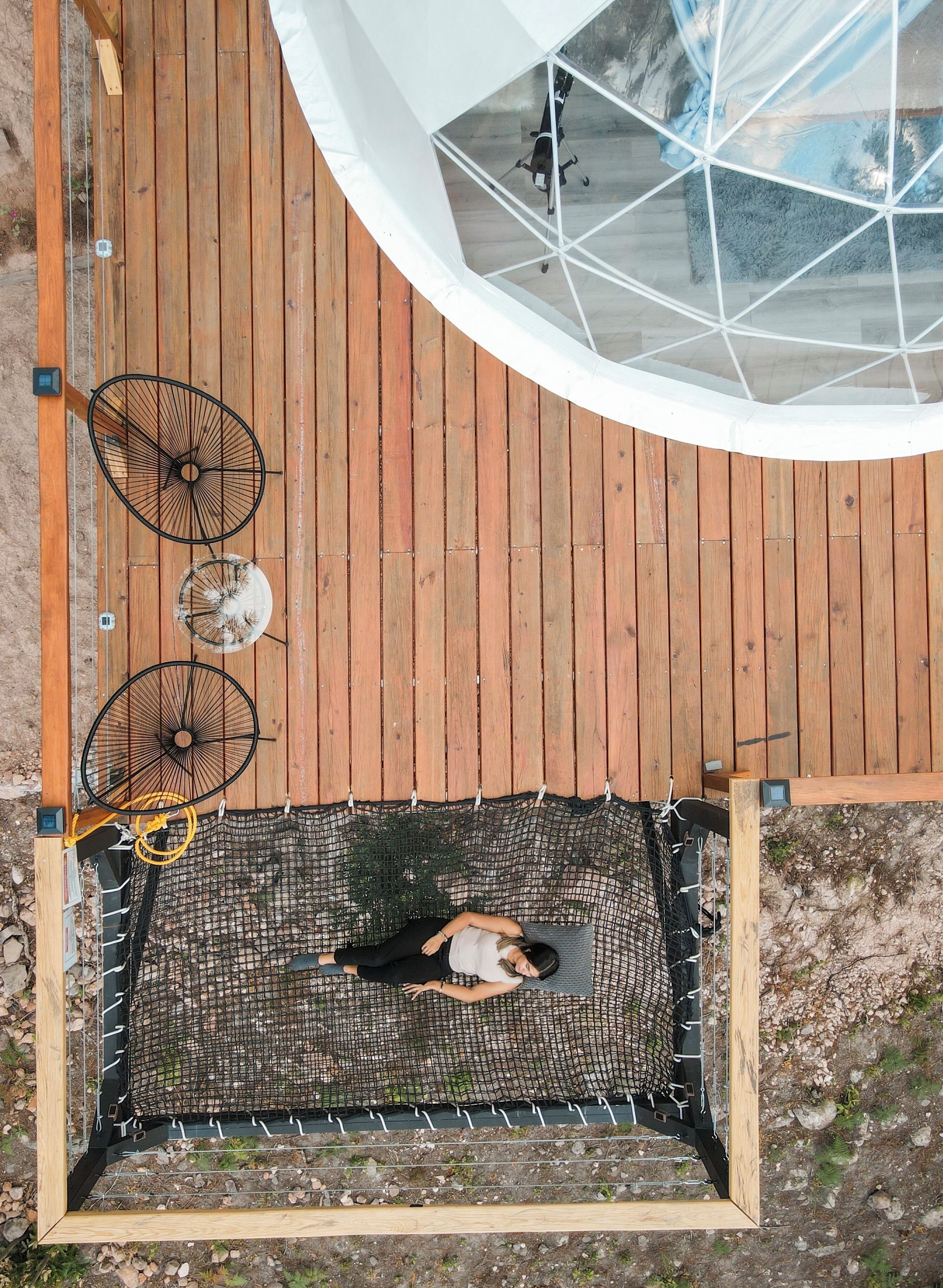 A hammock suspended between two wooden posts on a wooden deck, with a circular glass structure above.