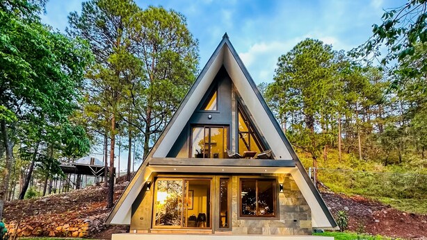 A modern house with a triangular roof, large windows, and a stone foundation.