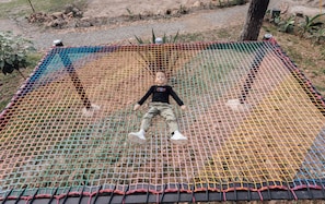 A child lying on a netted play area with a tree and rocks in the background.
