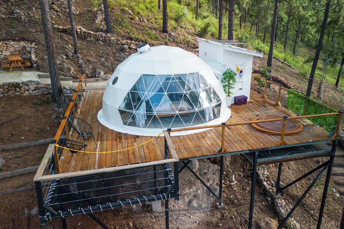 A geodesic dome structure with a wooden deck and a small building attached.