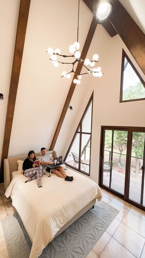 A bedroom with a large bed, a chandelier, and a view of the outdoors through a window.