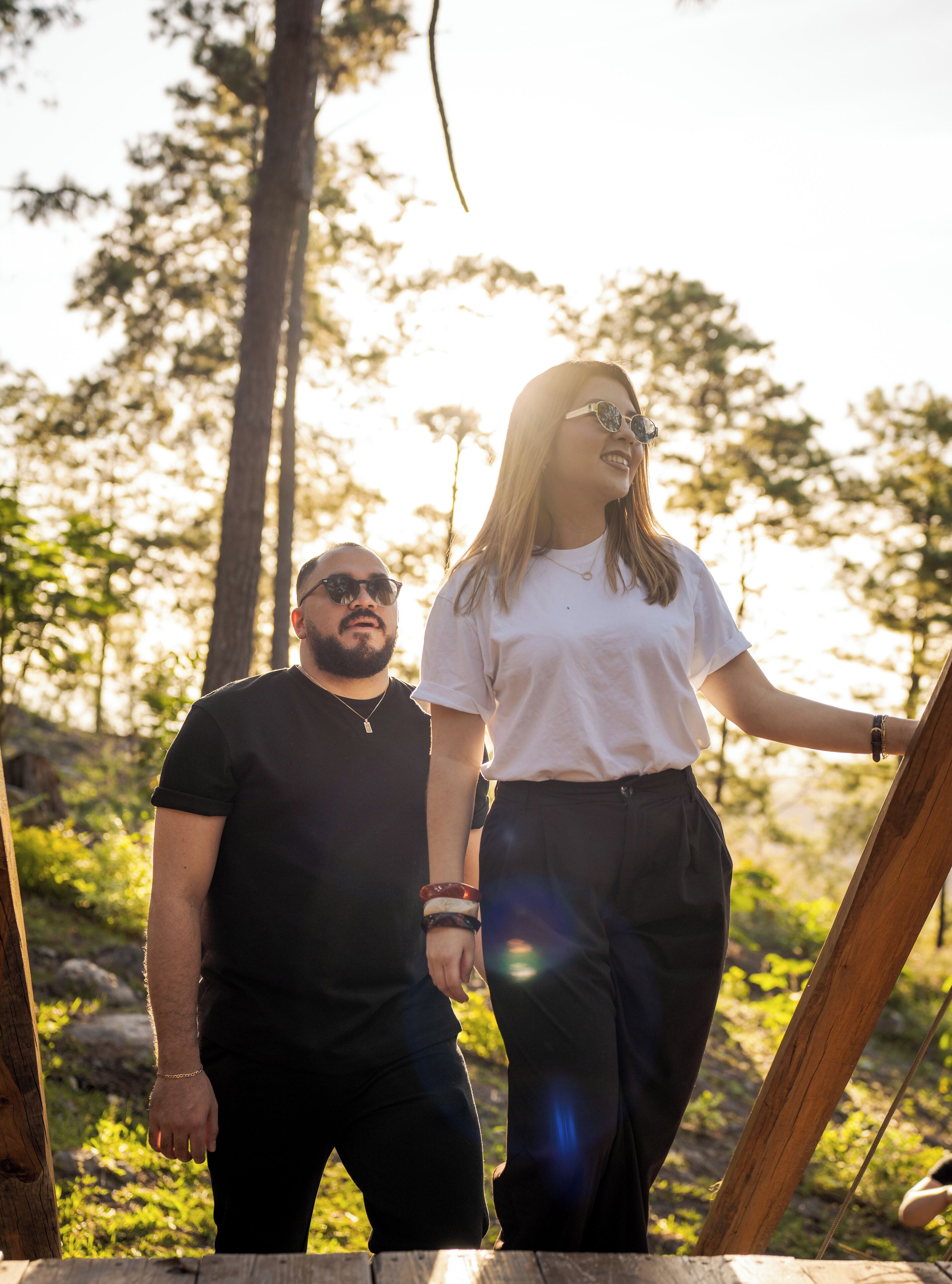 Two people standing on a wooden bridge with a forest background.