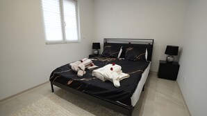 A neatly made bed with a black and white patterned bedspread, two bedside tables with lamps, and a window with blinds. - Le Marbre Blanc 4* - Les Suites du Lion (Rosheim)