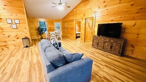 Interior de una cabaña de madera con sofá, televisión y zona de comedor.