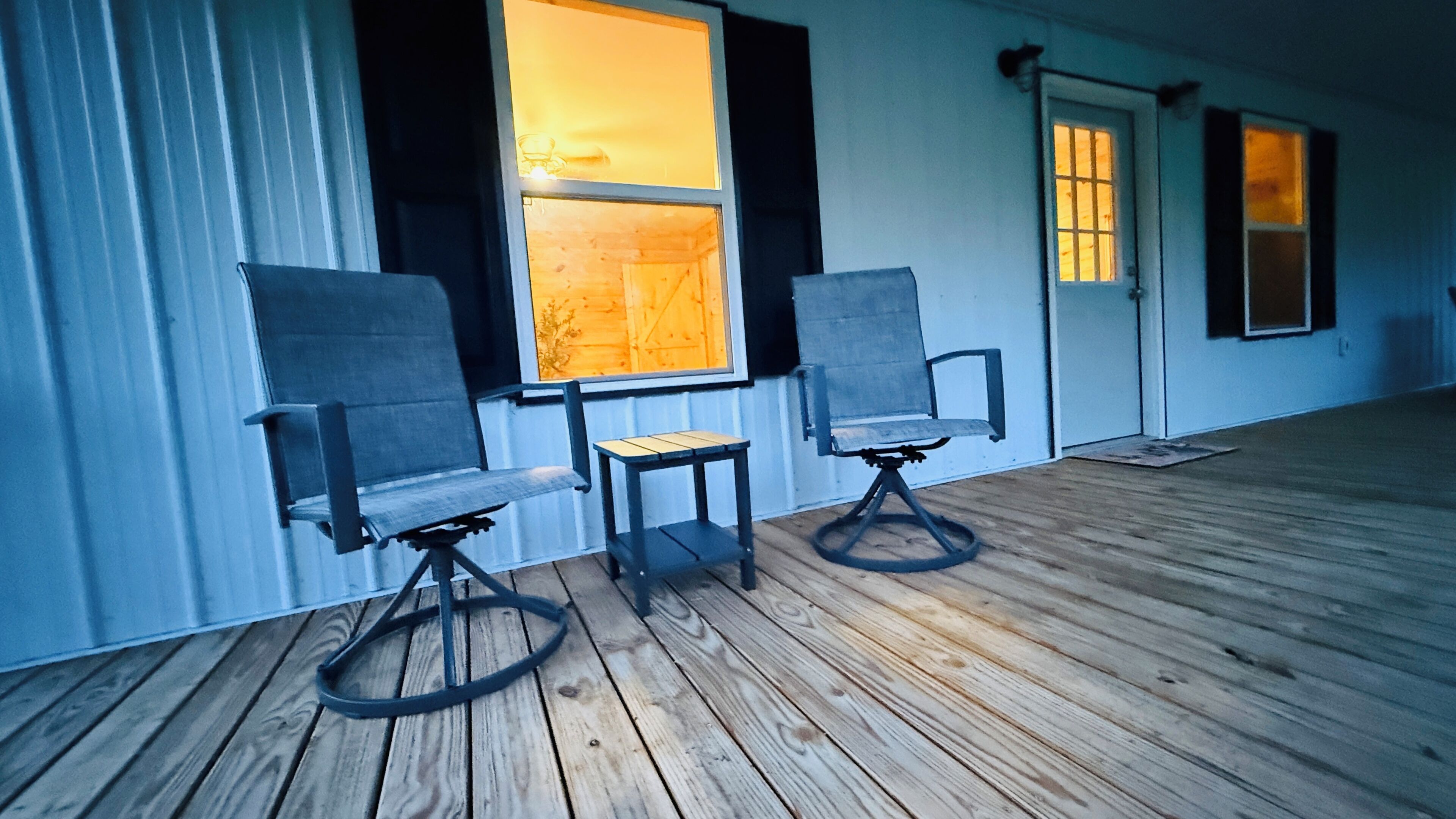 A room with two chairs and a small table on a wooden floor, with windows allowing natural light.