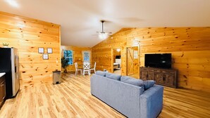 Interior de una cabaña de troncos con sofá, televisor y paredes de madera.