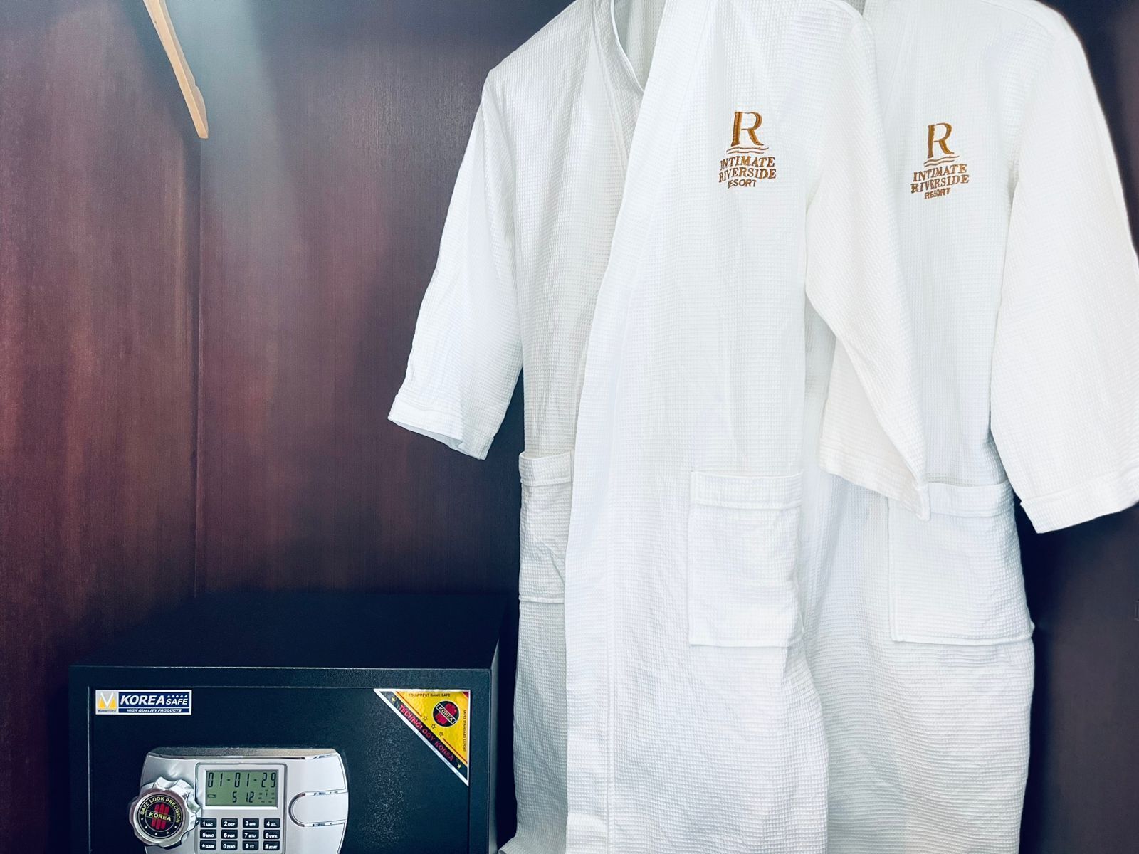 Two white robes with 'Intimate Riverside Resort' embroidered on them, hanging on a dark wooden wall.