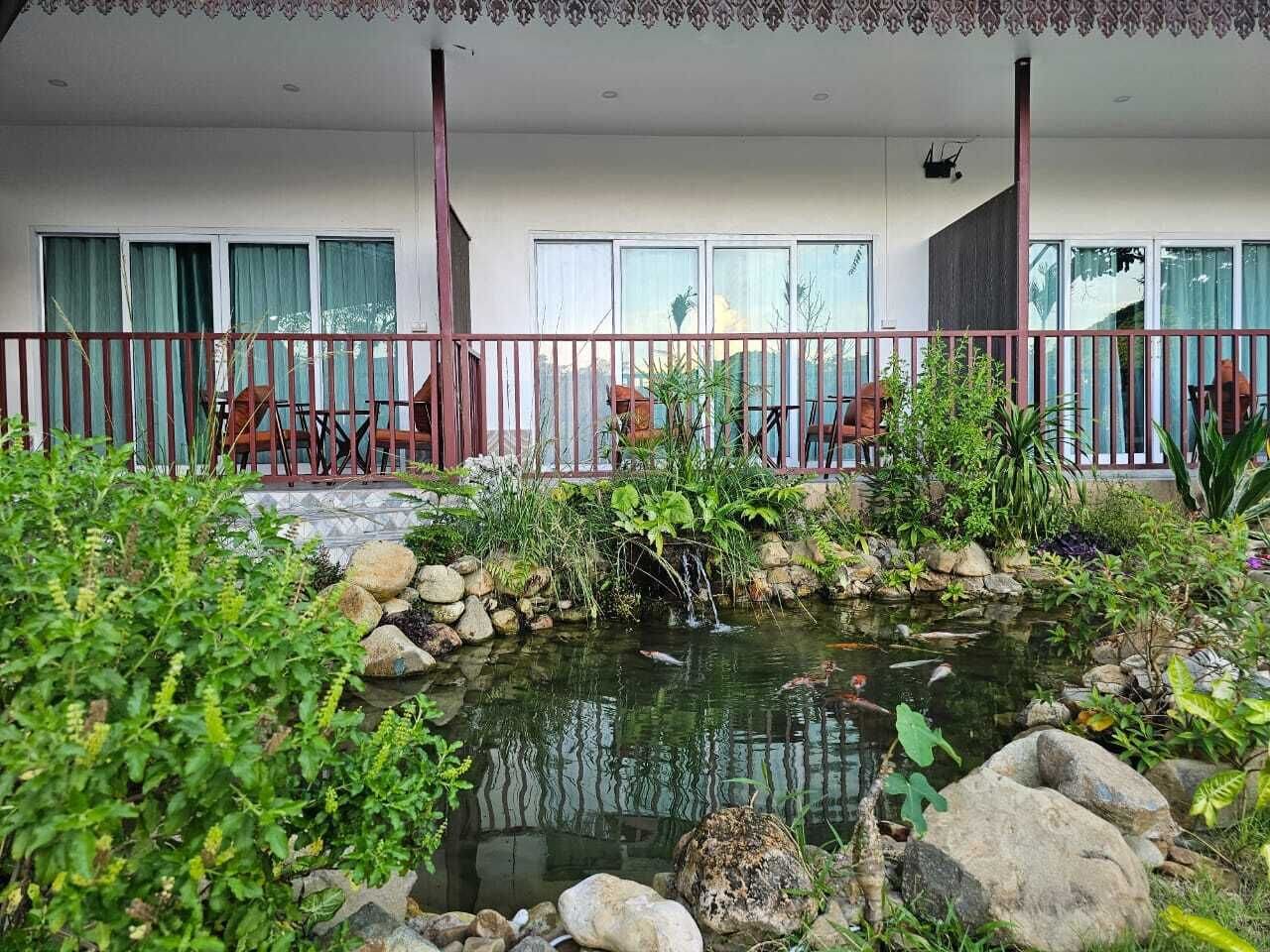 A balcony with a small pond, surrounded by rocks and plants, and a seating area with chairs.