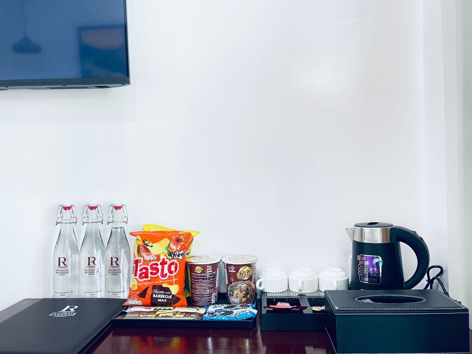 Habitación de hotel con minibar que incluye botellas de agua, una bolsa de chips Tostitos, una lata de café y una tetera.