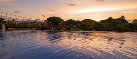 A swimming pool with a view of a bridge and trees at sunset.