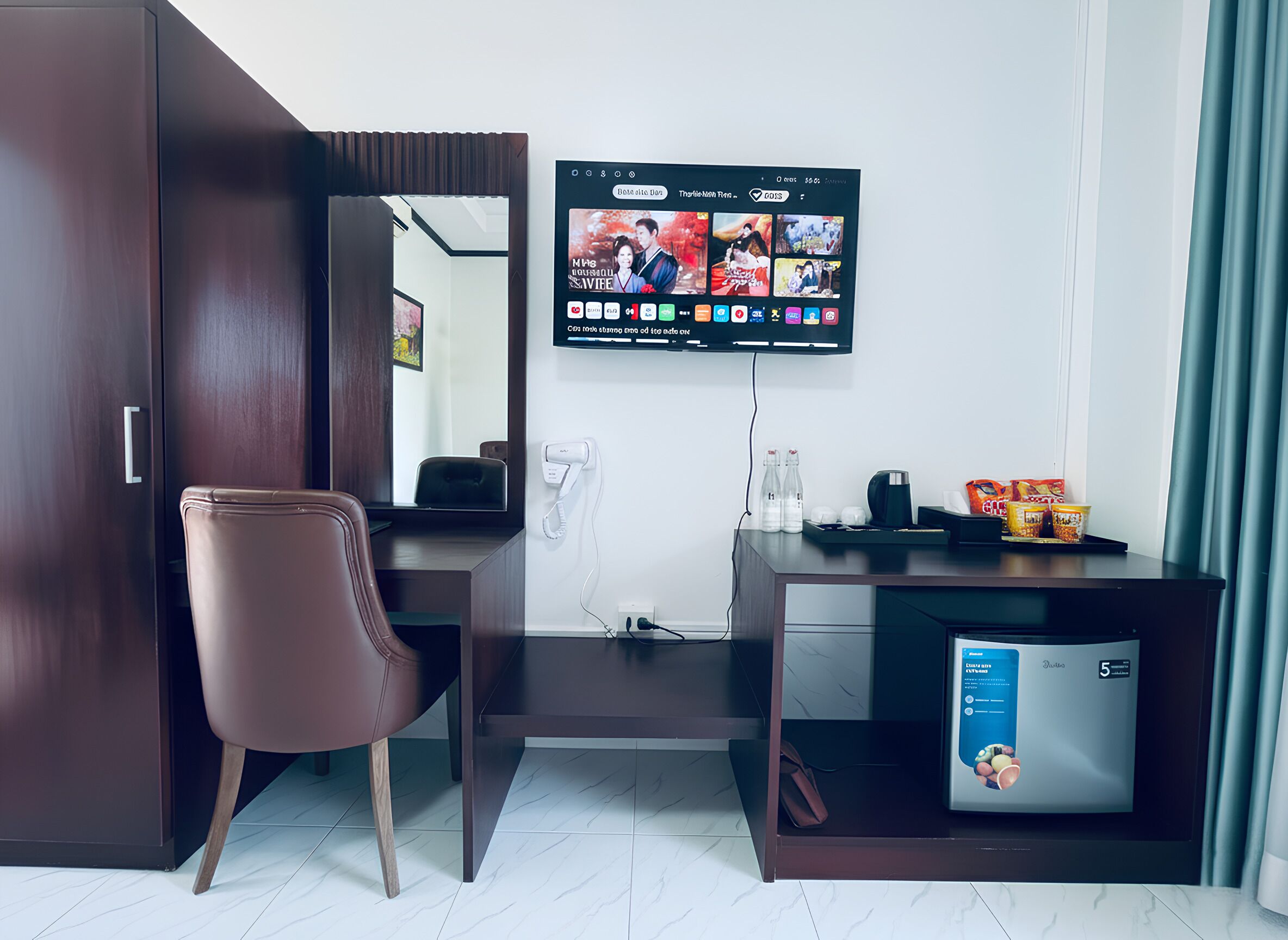 A hotel room with a desk, chair, television, and a minibar.