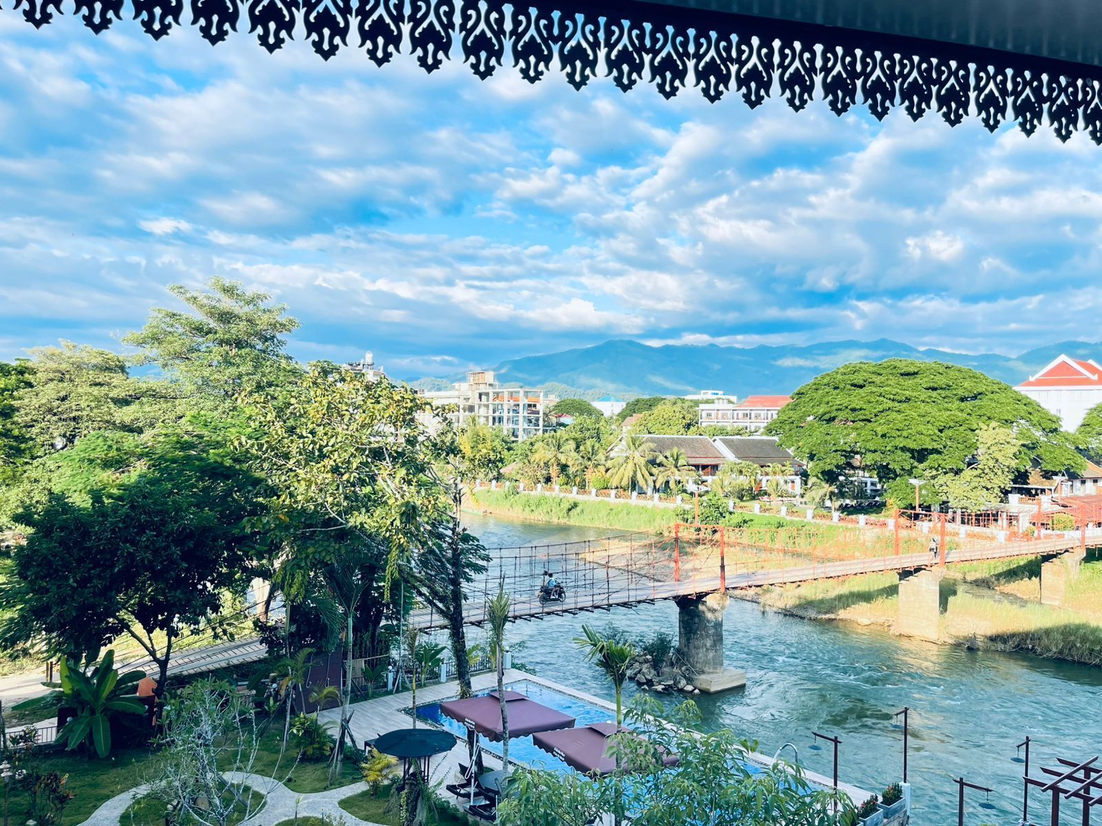 Vista junto al río con un puente, vegetación y edificios al fondo.