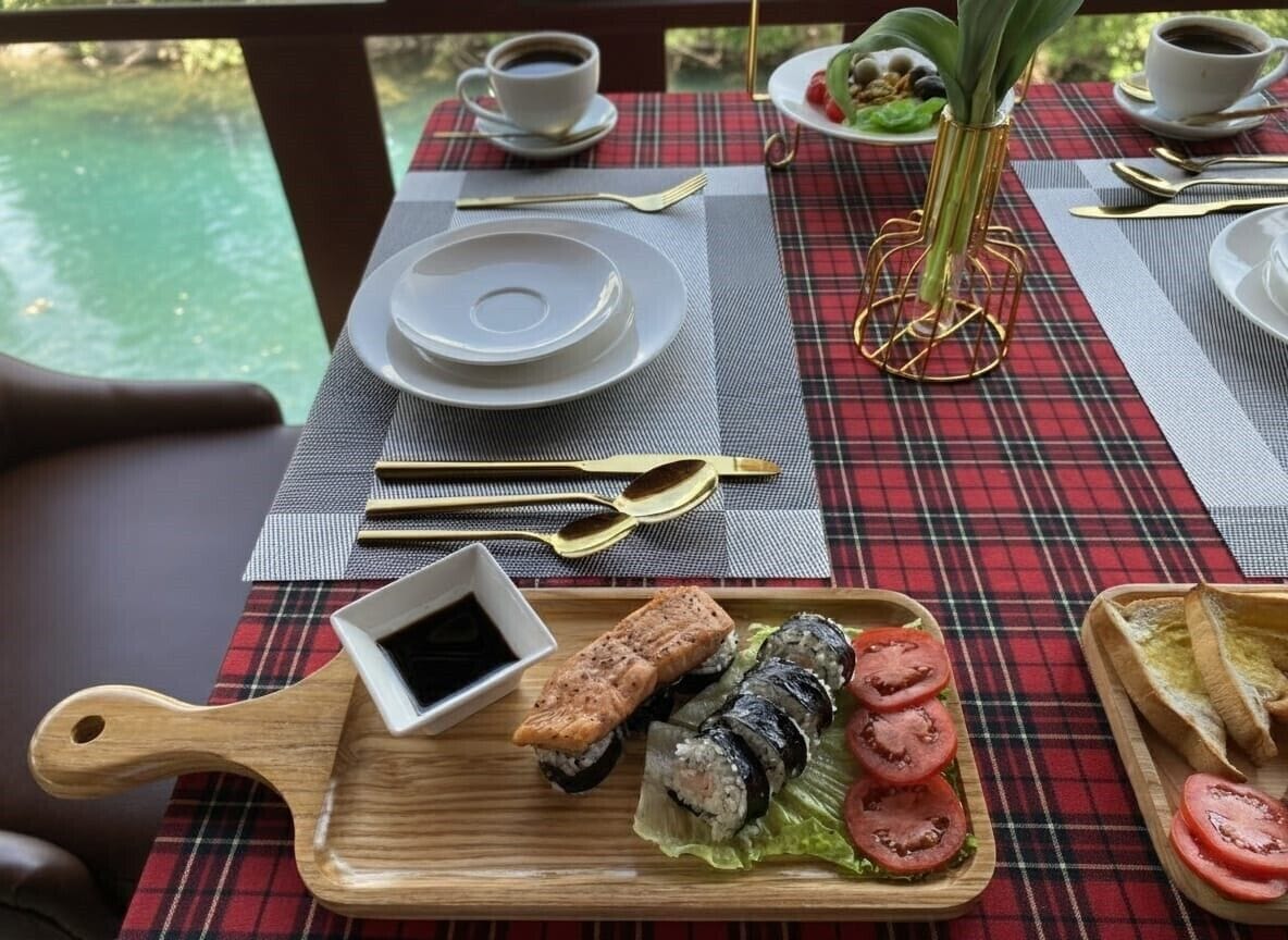 A table set with a red and black checkered tablecloth, plates, cutlery, and a wooden serving tray with sushi and a small dish of soy sauce.