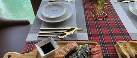 Una mesa dispuesta con mantel a cuadros rojo y negro, platos, cubiertos y una bandeja de madera con sushi y un recipiente pequeño de salsa de soja.