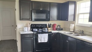 A kitchen with dark cabinets, a microwave, a stove, and a sink. - Sunset Family Point (Independence)