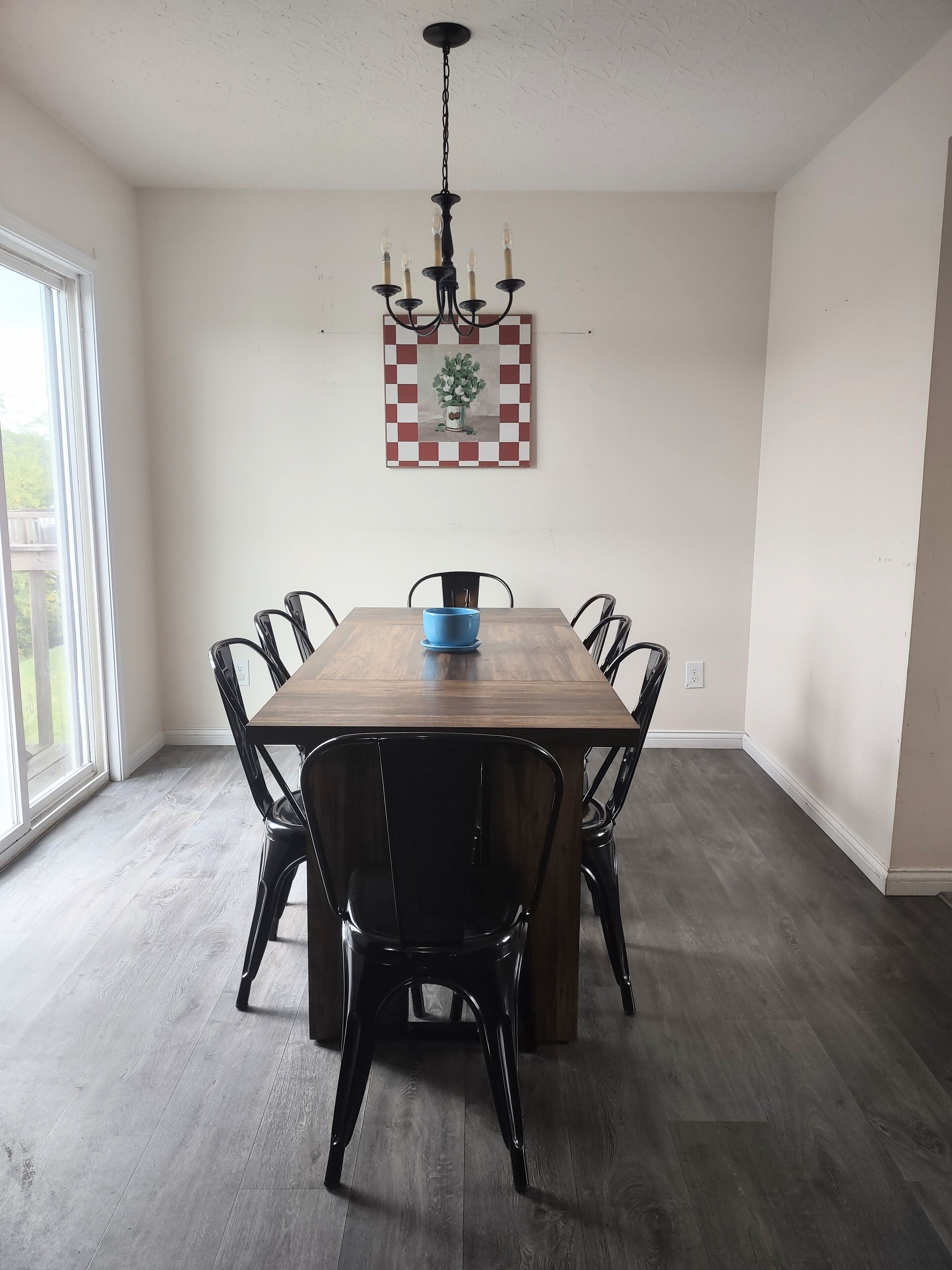 Un coin repas avec une table en bois, des chaises noires, un bol bleu et un lustre.