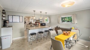 Cocina compacta con una isla central, taburetes de bar y una mesa de comedor con mantel amarillo.
