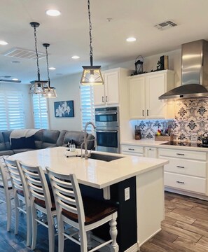 A modern kitchen with a central island, white cabinetry, stainless steel appliances, and a decorative backsplash. - Cozy Desert Winter Haven (Peoria)