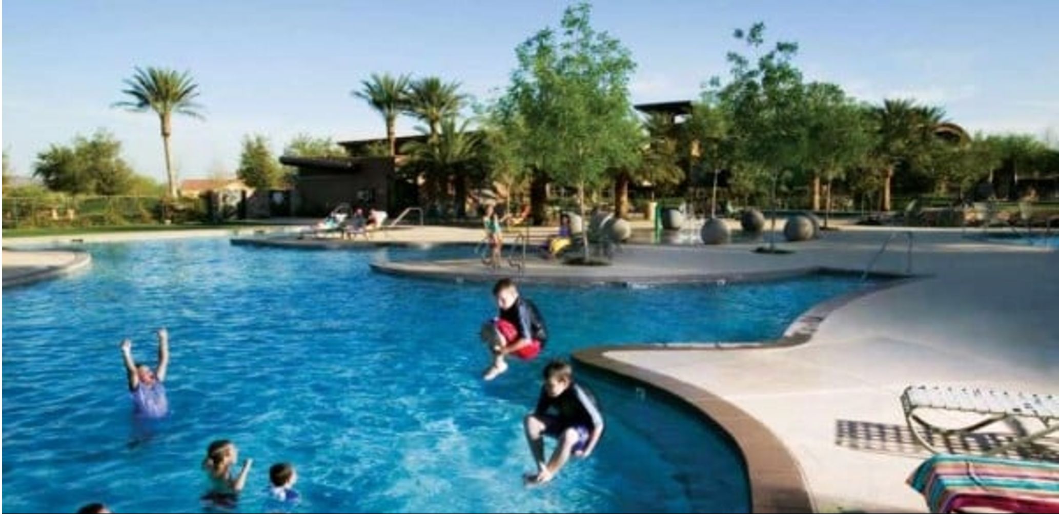 A swimming pool area with multiple lanes, palm trees, and a lounge chair.