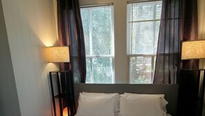A neatly made bed with white bedding, two bedside lamps, and a window with blinds. - Duck Pond Getaway (Gainesville)