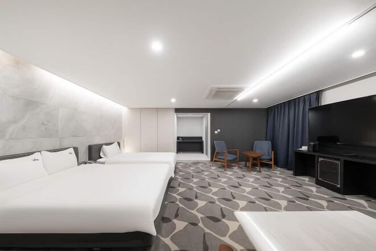 A hotel room with two beds, a TV, a desk, and a seating area.