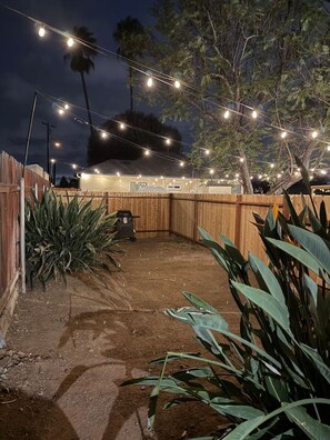 A backyard with a wooden fence, string lights, and a barbecue grill. - Comfy Sundance Casa • AC • Grill • Yard • Central (La Mesa)