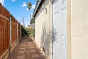A narrow pathway leading to a white garage door, flanked by a wooden fence and a stucco wall.