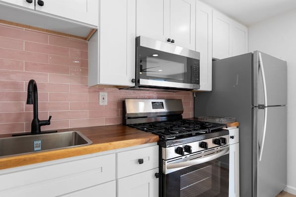 A kitchen with white cabinets, a stainless steel stove, a microwave, and a refrigerator.