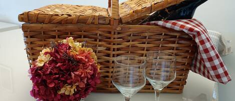 A wicker picnic basket with a bottle and two wine glasses on a white table.