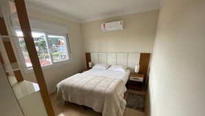 Une chambre à coucher comprenant un lit, des tables de chevet, une fenêtre et un appareil de climatisation.