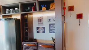 Une cuisine équipée d’un réfrigérateur en acier inoxydable, de deux tabourets de bar et d’un mur décoré d’œuvres d’art sur le thème du café.