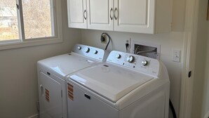 A laundry room with two white front-loading washers, a window, and white cabinetry above. - Coming for work?! Stay here! (Rock Springs)