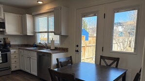 A kitchen with white cabinets, a dishwasher, a sink, and a dining area with a table and chairs. - Coming for work?! Stay here! (Rock Springs)