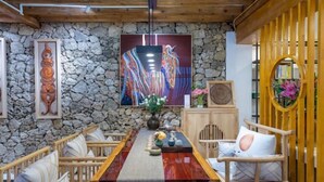 A dining area with a stone wall, wooden chairs, a long wooden table, and a large painting above the table. - Lijiang Muyuntang View Hotel (Lijiang)
