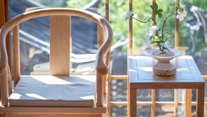 A wooden chair with a cushion, a small table with a potted plant, and a window with a view of greenery. - Lijiang Muyuntang View Hotel (Lijiang)