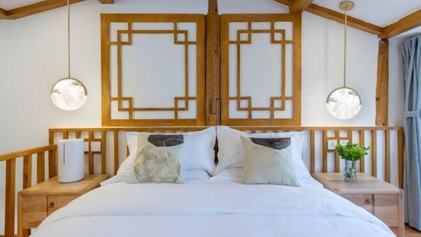 A bedroom with a wooden headboard, a bed with white bedding, two bedside tables with lamps, and a window with curtains. - Lijiang Muyuntang View Hotel (Lijiang)