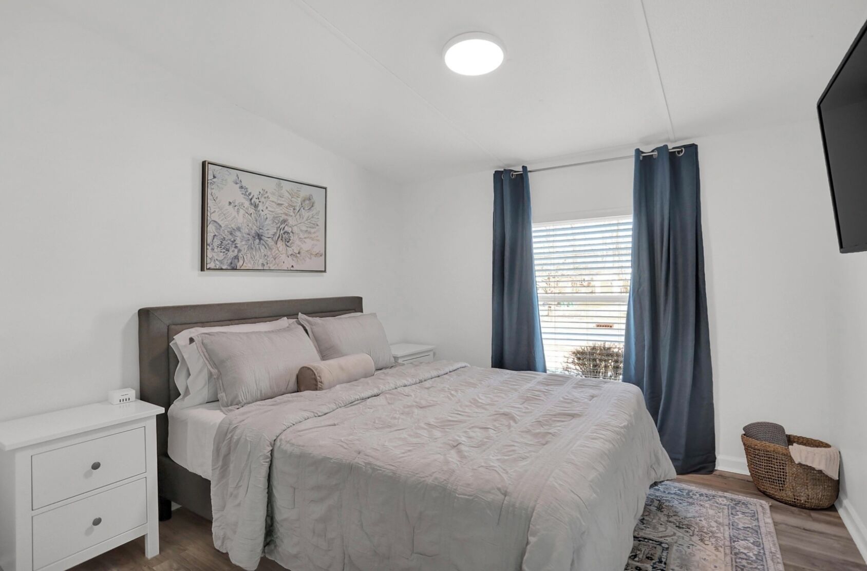 Een slaapkamer met een bed, nachtkastje en een kunstwerk aan de muur.