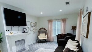 A living room with a flat-screen TV, a fireplace, a sofa, and a chair. - Corporate Ready 2BR Bungalow | W/D • Workspace • Wi-Fi • Long Stay (Atlanta)