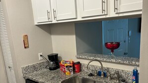 Una cocina con armarios blancos, encimera de granito, pileta de acero inoxidable y lavavajillas.