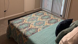 A bedroom with a bed, a ceiling fan, a TV mounted on the wall, and a window with blinds.