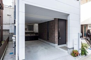 A modern building entrance with a covered driveway, a black door, and a visible kitchen area.