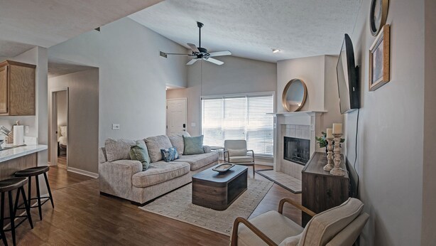A spacious living room with a fireplace, a ceiling fan, and a kitchen area visible in the background. - Contemporary Retreat near Lakeshore (Brandon)