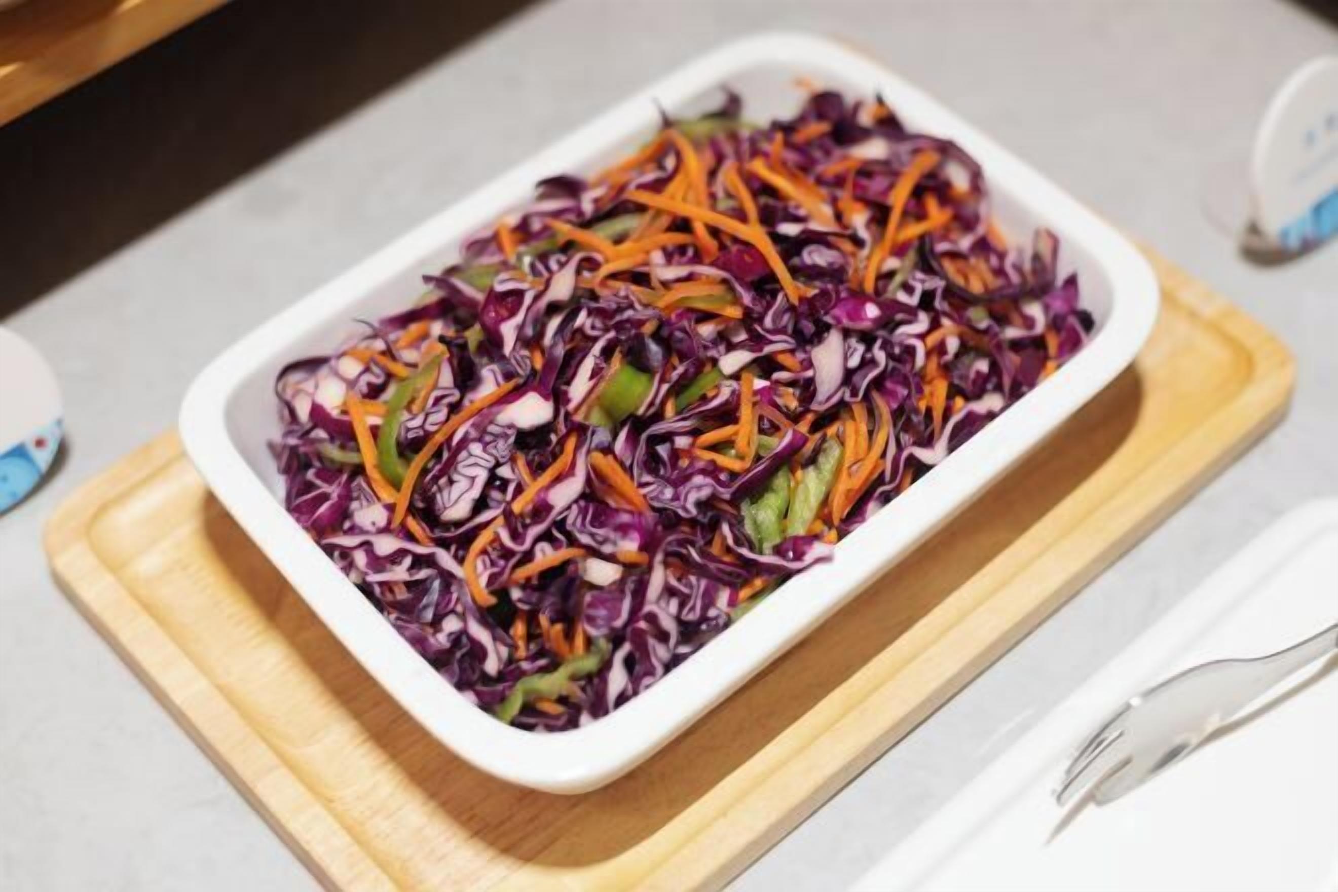 A white rectangular dish filled with a colorful salad on a wooden board.