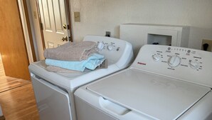 A compact laundry area with a front-loading washer and dryer, wooden cabinets above, and a door leading to another room.