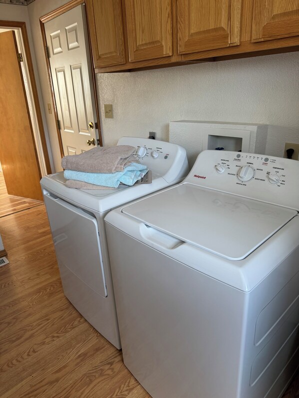 A compact laundry area with a front-loading washer and dryer, wooden cabinets above, and a door leading to another room.