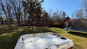 A hot tub with a marble exterior, surrounded by a grassy yard and trees. - Upscale Mountain Cottage with Hot Tub & Fireplace (Long Pond)