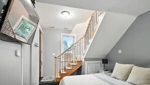 A bedroom with a bed, a nightstand, a lamp, a window, and a staircase leading to an upper floor. - HotTub~Gym~Fire Pit~5 Min to Mass Ave~Spacious for Groups~Indianapolis (Indianapolis)