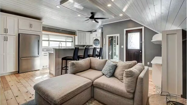 A modern kitchen with white cabinets, a stainless steel refrigerator, and a dining area with a bar stool. - HotTub~Gym~Fire Pit~5 Min to Mass Ave~Spacious for Groups~Indianapolis (Indianapolis)