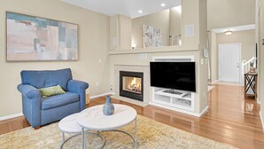 Ein Wohnzimmer mit Kamin, Fernseher, blauem Sessel und einem Marmortisch.