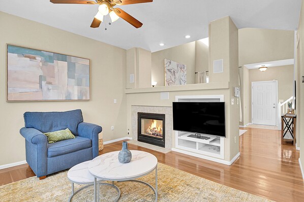A living room with a fireplace, a television, a blue armchair, and a marble coffee table. - Spacious Comfort Near DIA (Aurora)